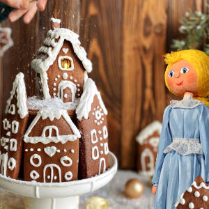 Grafika przedstawia paterę z piernikami w kształcie domków z białym lukrem oraz lalkę teatralną 