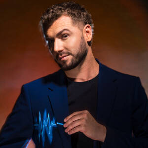 Zdjęcie portretowe Kamila Bednarka. Na marynarce artysty po stronie serca narysowana jest linia dźwięku