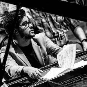 Zdjęcie czarno białe. Przy foretpianie siedzi pianista i przegląda nuty.