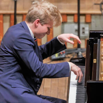 Zdjęcie przedstawia grającego na fortepianie pianistę