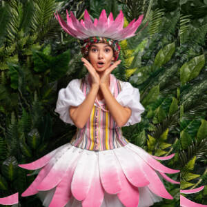 Grafika przedstawia kolorowe zdjęcie, na zdjęciu widzimy aktorkę przebraną za biało-różowy kwiat