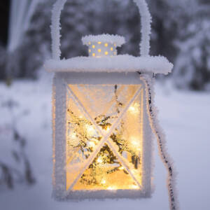 Grafika przedstawia zaśnieżony biały lampion z ciepłymi światełkami w środku