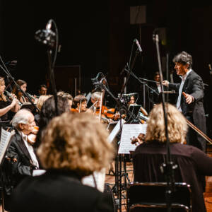 Zdjęcie przedstawia orkiestrę symfoniczną wraz z dyrygentem