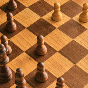 Grafika przedstawia drewnianą szachownicę i szachy