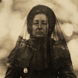 Na zdjęciu w sepii widać kobietę ubraną w suknię z wieku dziewiętnastego, na głowie ma okrycie żałobne, na dłoniach koronkowe czarne rękawiczki. W dłoniach trzyma ramkę ze zdjęciem powstańca