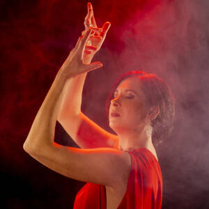 Grafika przedstawia tańczącą kobietę w czerwonej sukni w dymie i w czerwonym świetle