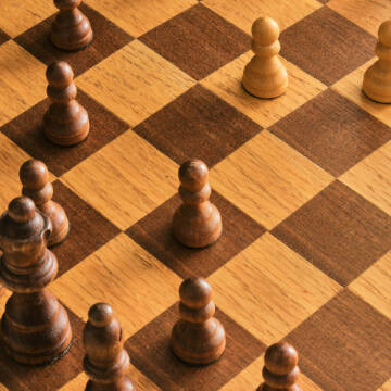 Grafika przedstawia drewnianą szachownicę z pionkami
