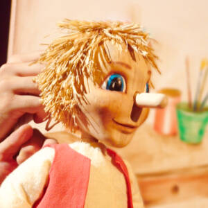 Grafika przedstawia drewnianą lalkę teatralną z długim nosem